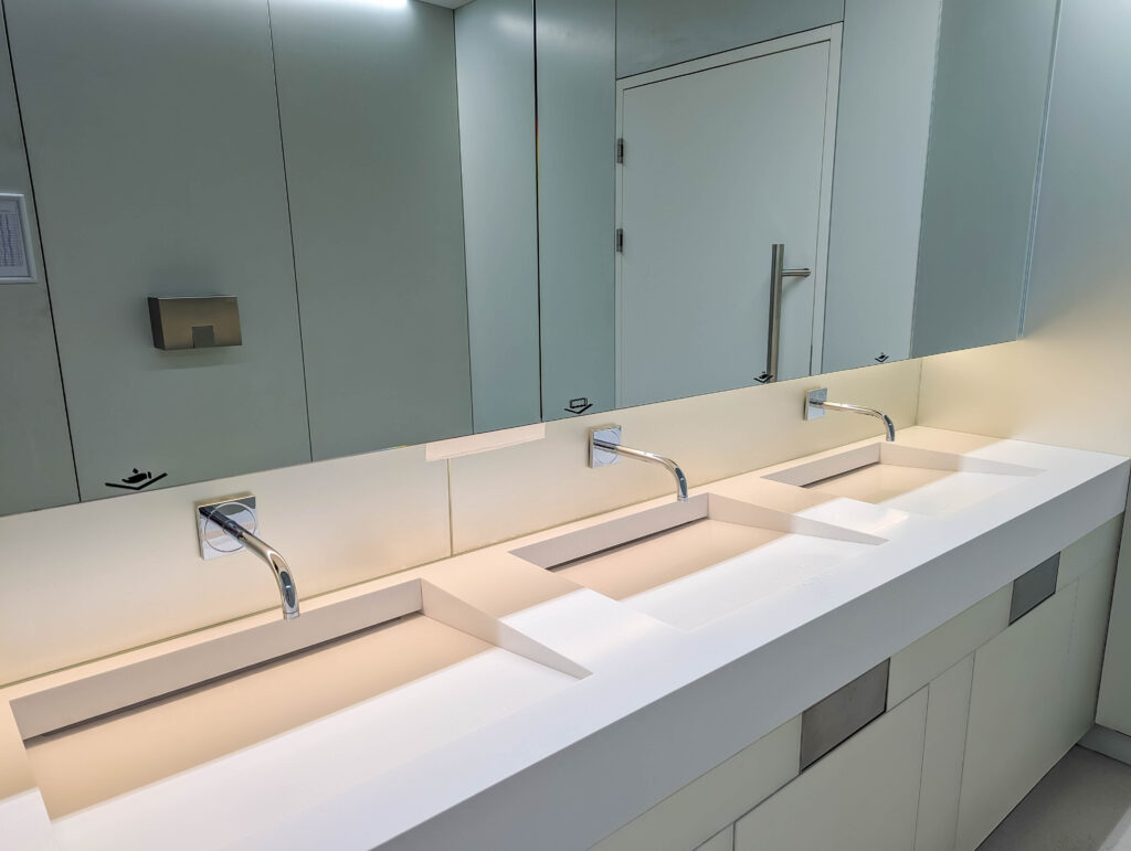 Long row of modern bathroom sinks with mirrors in bright white public restroom facility